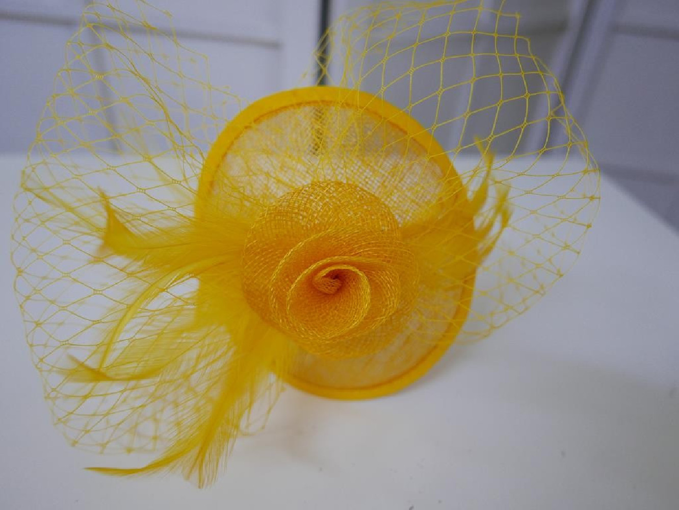 Żólty fascynator z sinamay z woalką i piórami na przepasce