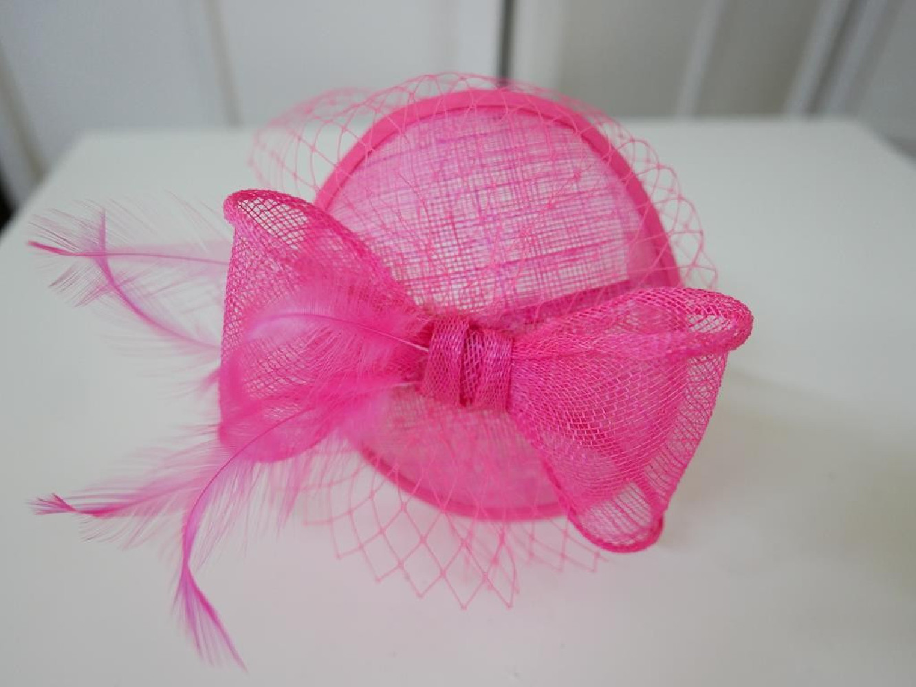 Różowy fascynator z sinamay z woalką i piórami na przepasce