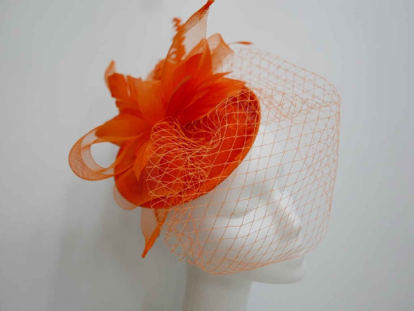 Pomarańczowy fascynator z sinamay z woalką i piórami na przepasce