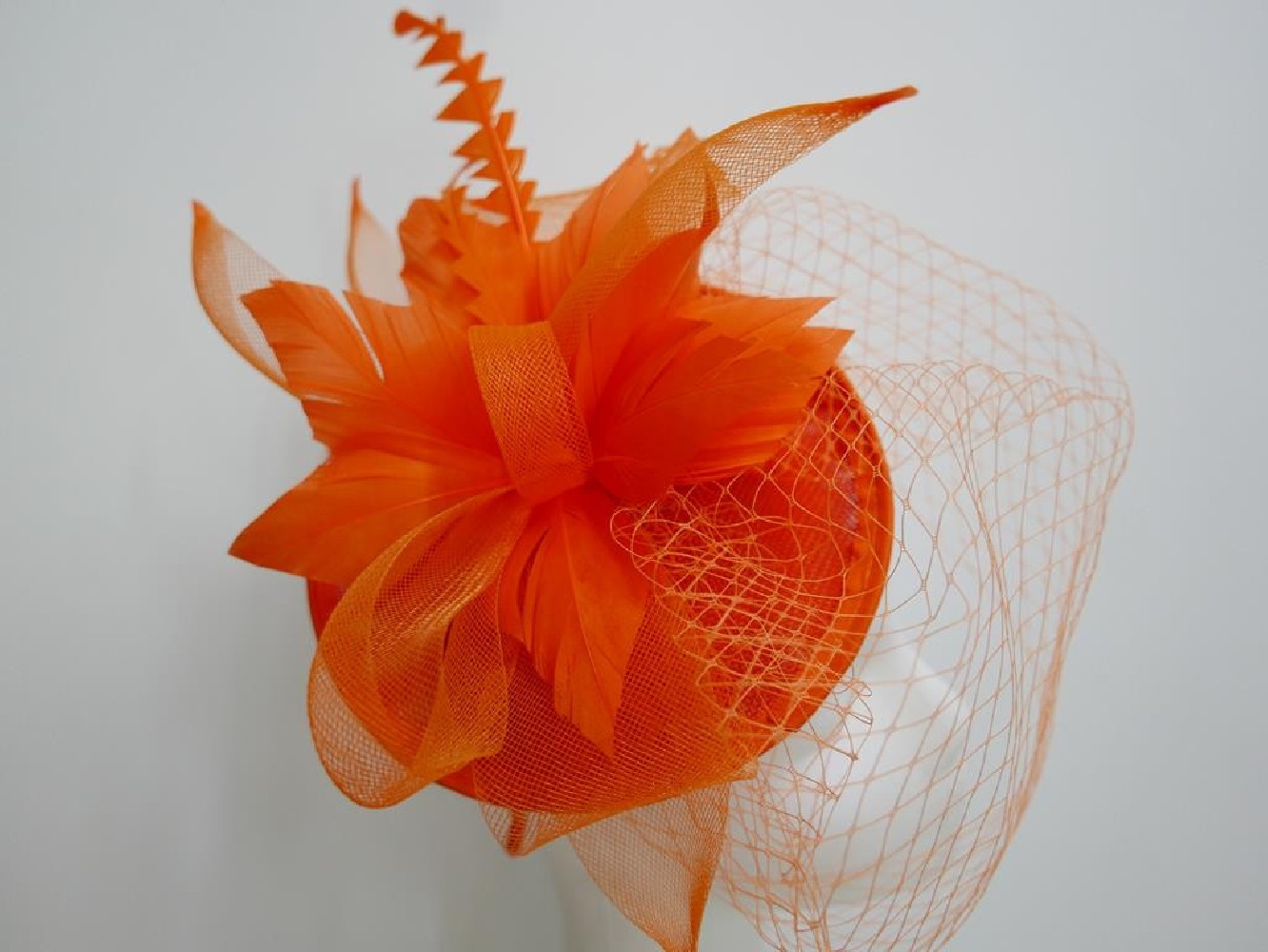 Pomarańczowy fascynator z sinamay z woalką i piórami na przepasce