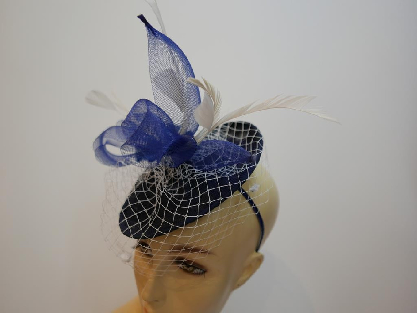Granatowo śmietankowy fascynator z piórami i woalką na przepasce