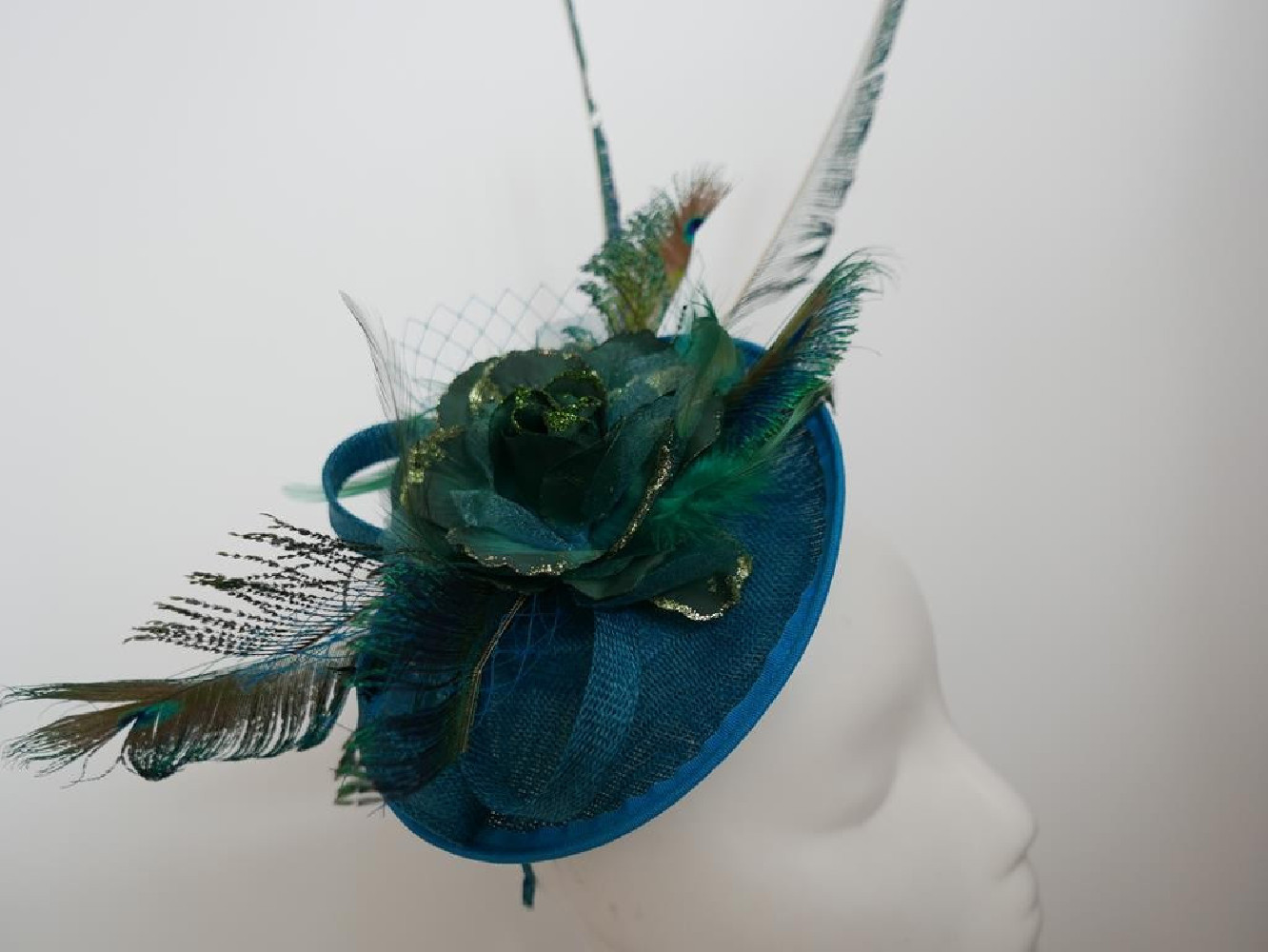 Turkusowo zielony fascynator z piórami i woalką na przepasce