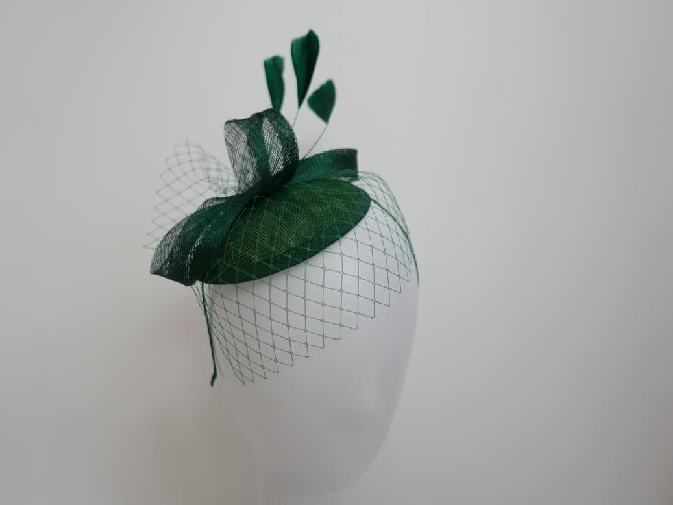 Zielony fascynator z woalką i piórami na przepasce