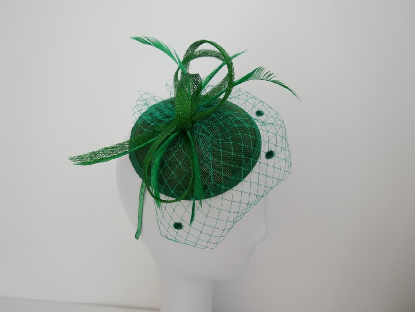 Zielony fascynator z woalką i piórami na przepasce