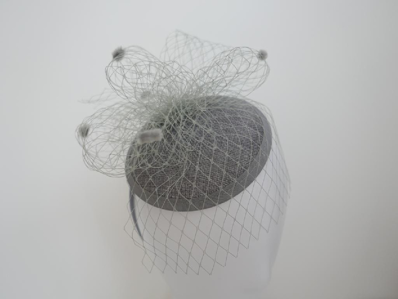 Szary fascynator z woalką i piórami na przepasce