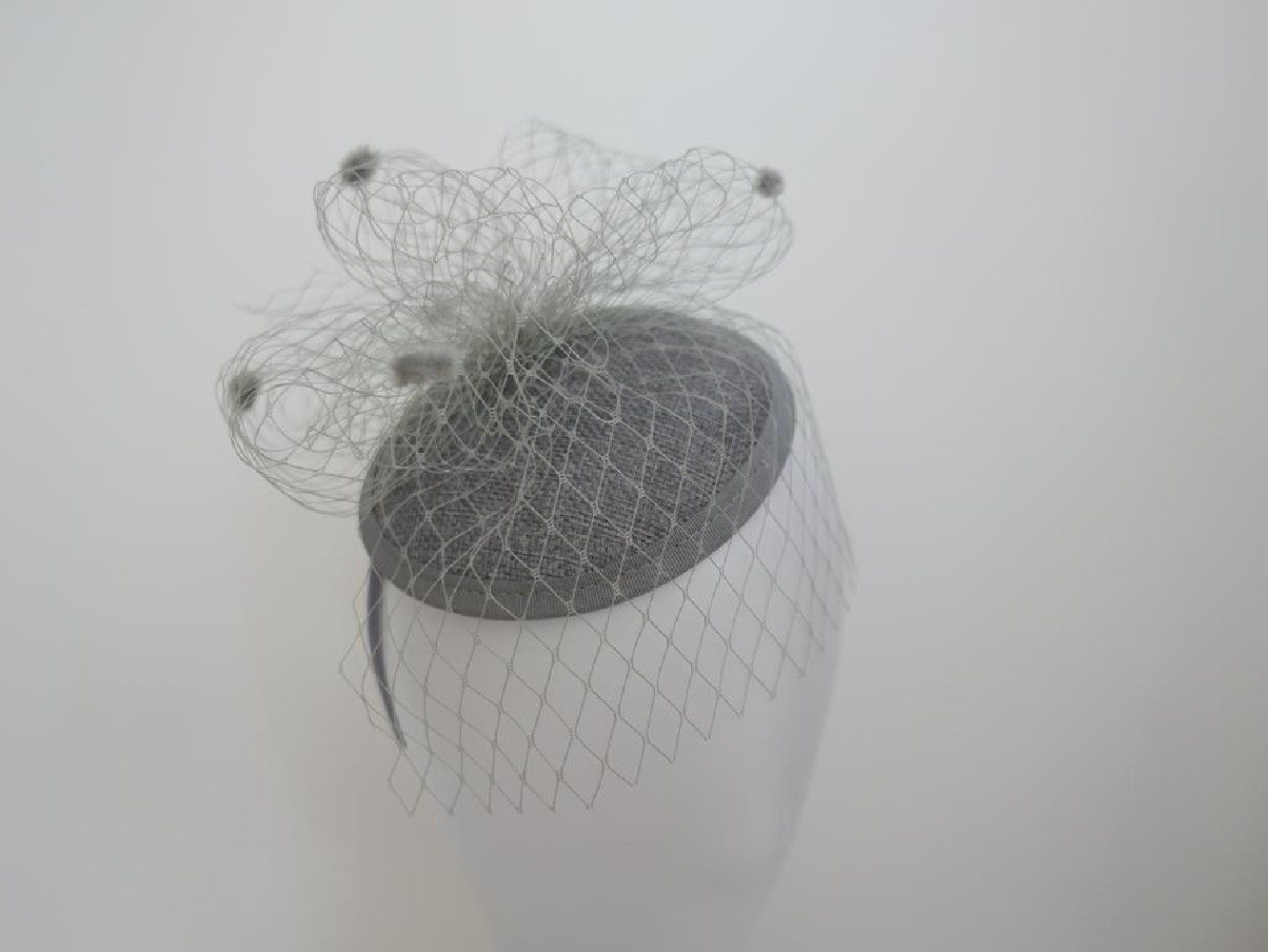 Szary fascynator z woalką i piórami na przepasce