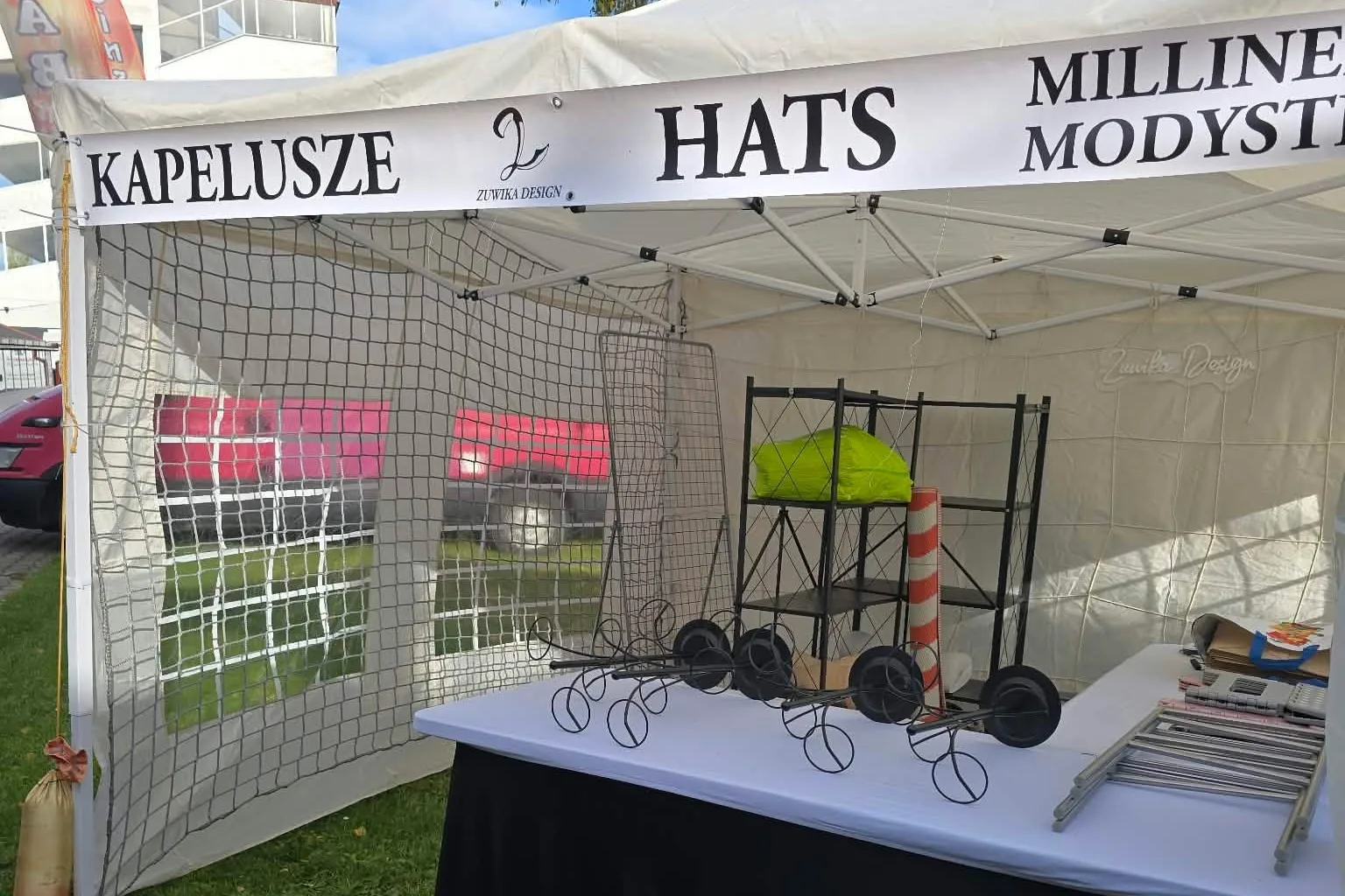 Namiot Zuwika Design z napisem Kapelusze, Hats, Millinery, Modystka: stół i stojaki przed rozłożeniem kapeluszy.