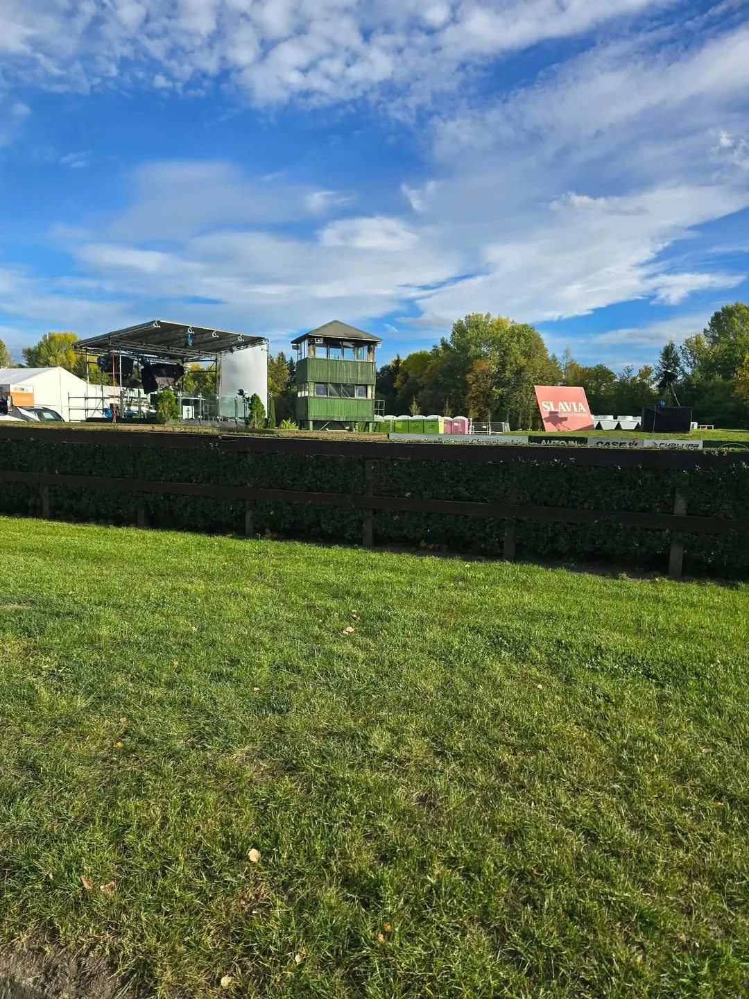 Żywopłot przy torze w Pardubicach, w tle wieża i scena przygotowane na wyścigowy weekend.